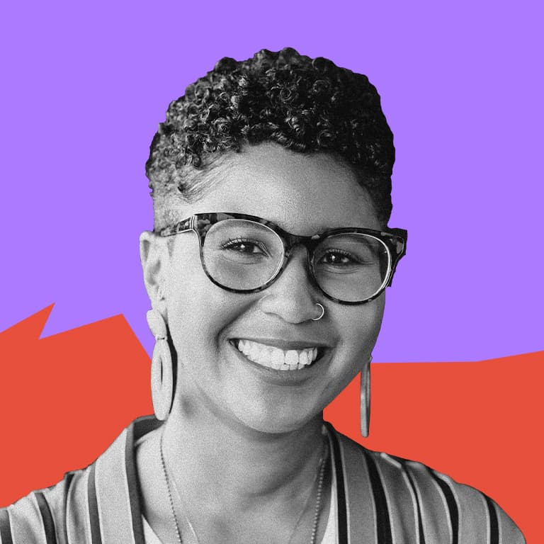 A young, African American woman with a short tapered fade, wearing large framed glasses and smiling.