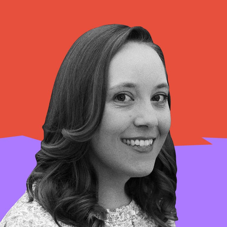 A smiling woman wearing a shirt patterned with hot air balloons, sitting in front of a purple wall.