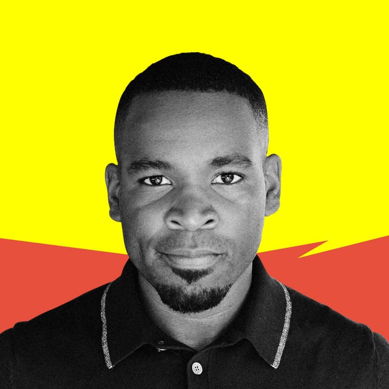 A young Afro-Caribbean American man with glasses, smiling, short haircut with a fade and rounder face.