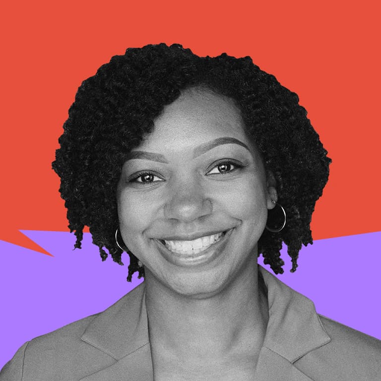 A young, African American woman wearing a cute pink blazer, pictured in front of a baby pink background, smiling at the camera.